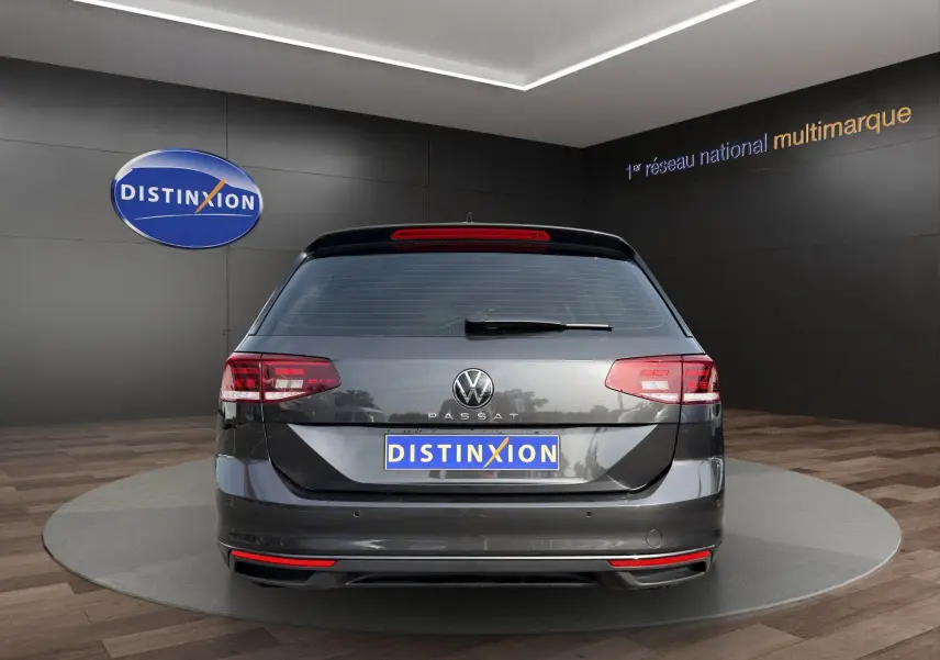 Vue arrière d'une Volkswagen Passat gris foncé 2022, avec feux LED et logo distinctif sur fond de showroom.