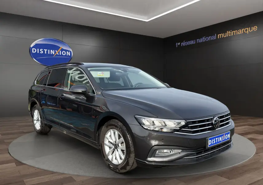 Volkswagen Passat break gris foncé vue 3/4 avant en intérieur avec jantes alliage et calandre chromée.