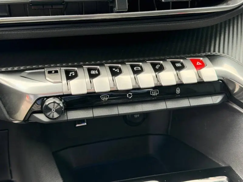 Gros plan sur la rangée de boutons argentés et noirs de la console centrale du Peugeot 3008 gris Titane, avec bouton rouge d'alerte.
