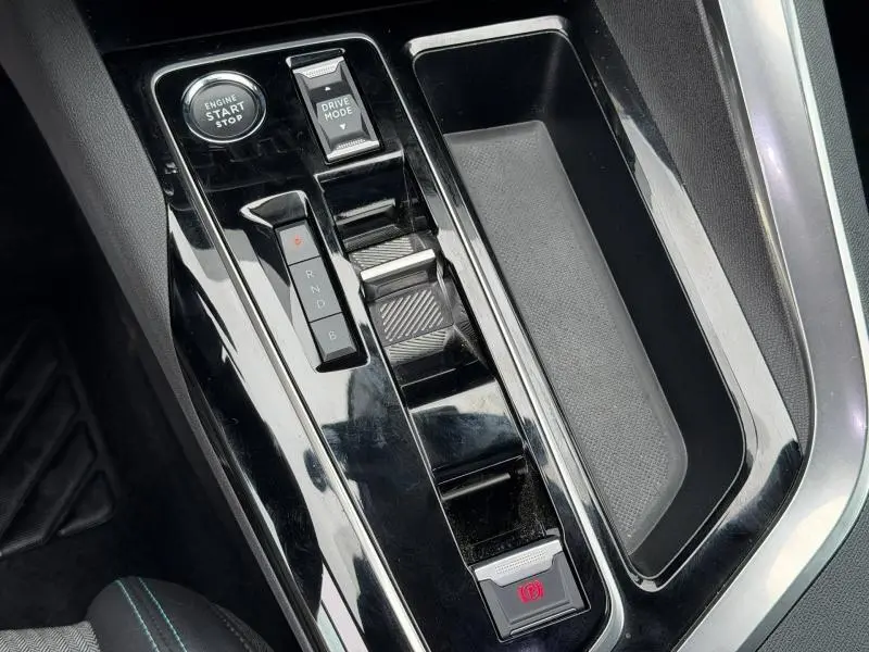 Gros plan sur la console centrale noire brillante du Peugeot 3008 Hybride Rechargeable 2024 avec boutons start, drive mode et frein à main électrique.