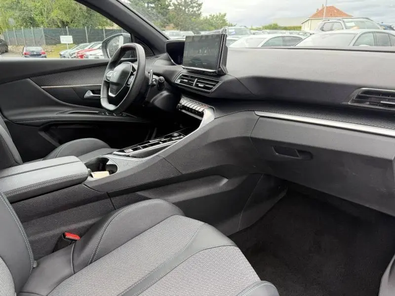 Vue intérieure côté conducteur du Peugeot 3008 hybride 2024, tableau de bord noir avec écran central tactile et volant cuir multifonction.