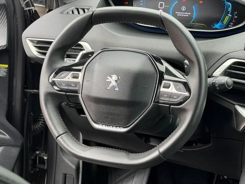 Vue rapprochée du volant cuir multifonction noir du Peugeot 3008 Hybride Rechargeable 2024 avec tableau de bord numérique bleu.
