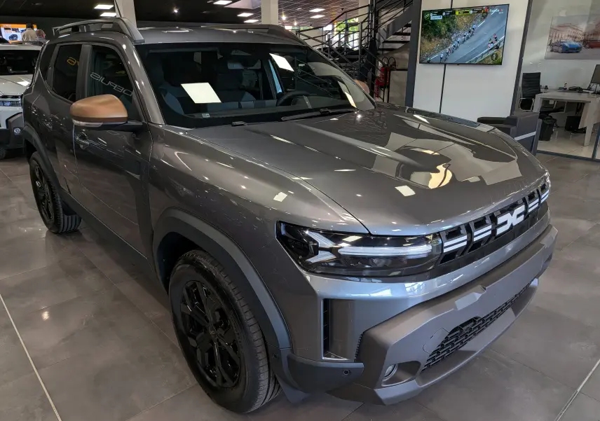 Dacia Duster 2026 gris schiste en vue 3/4 avant droit, avec rétroviseurs bronze et jantes noires brillantes.