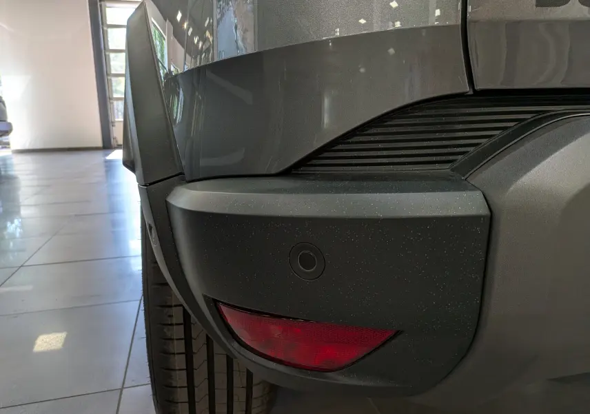 Gros plan sur l’angle arrière droit du Dacia Duster gris schiste, mettant en valeur le pare-chocs et le feu arrière.
