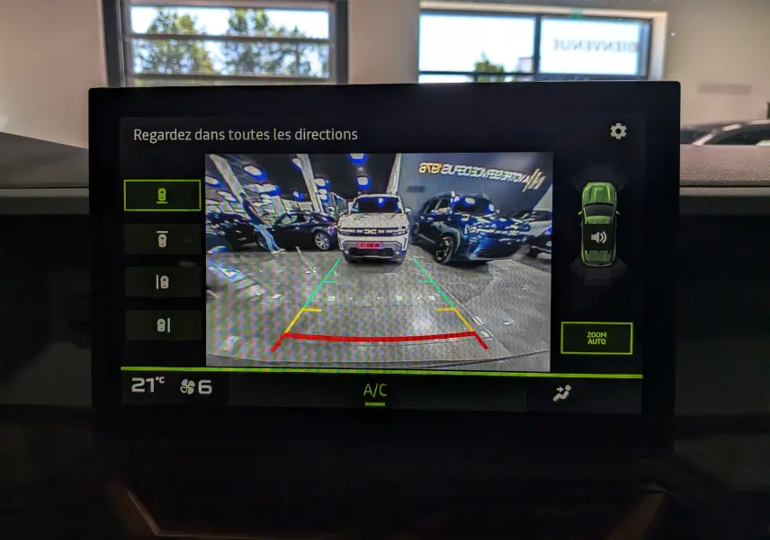 Vue arrière via caméra de recul montrant un Dacia Duster gris schiste garé dans un espace intérieur lumineux.