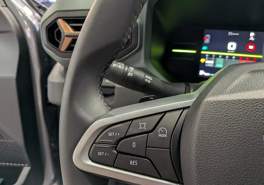 Gros plan sur le volant et commandes du DACIA Duster gris schiste, avec tableau de bord numérique en arrière-plan.