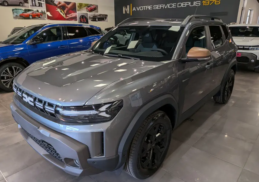 Vue 3/4 avant droite du Dacia Duster 2026 gris schiste avec rétroviseurs bronze et jantes noires en showroom.
