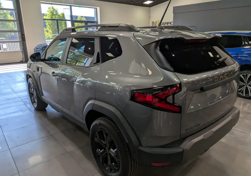 Vue 3/4 arrière droite du Dacia Duster 2026 gris schiste en showroom, avec feux arrière LED et jantes noires.