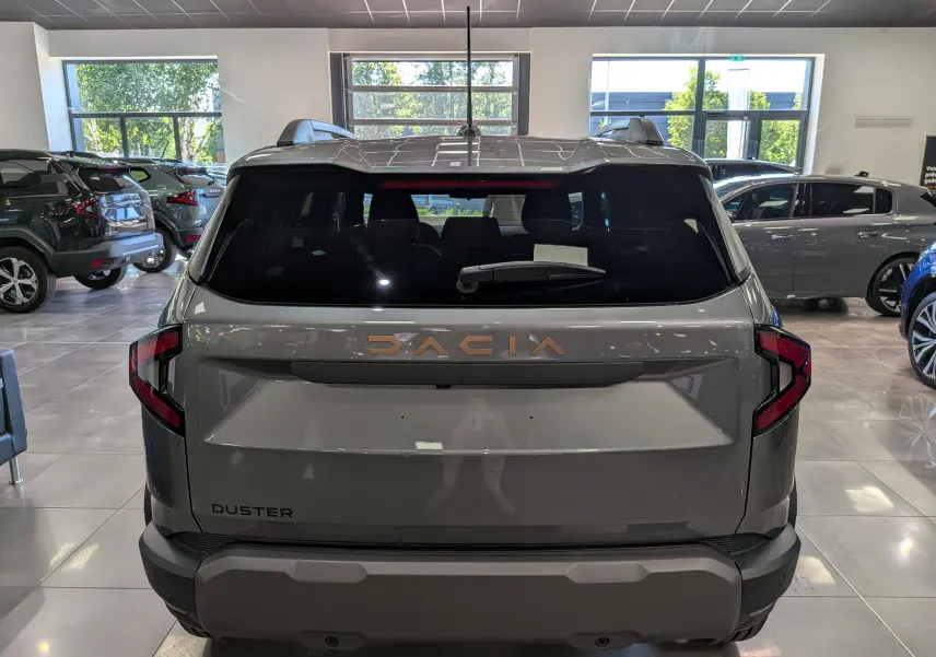Vue arrière d'un Dacia Duster 2026 gris schiste dans un showroom, avec logo DACIA en relief et feux arrière modernes.