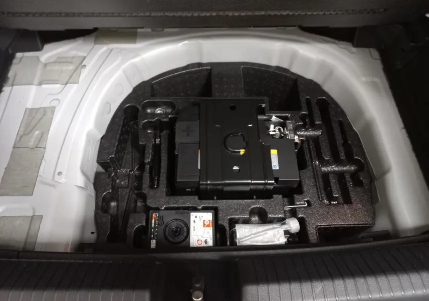 Vue plongeante sur le coffre ouvert d'une Volkswagen Polo blanche, montrant le compartiment à outils et la batterie de secours.