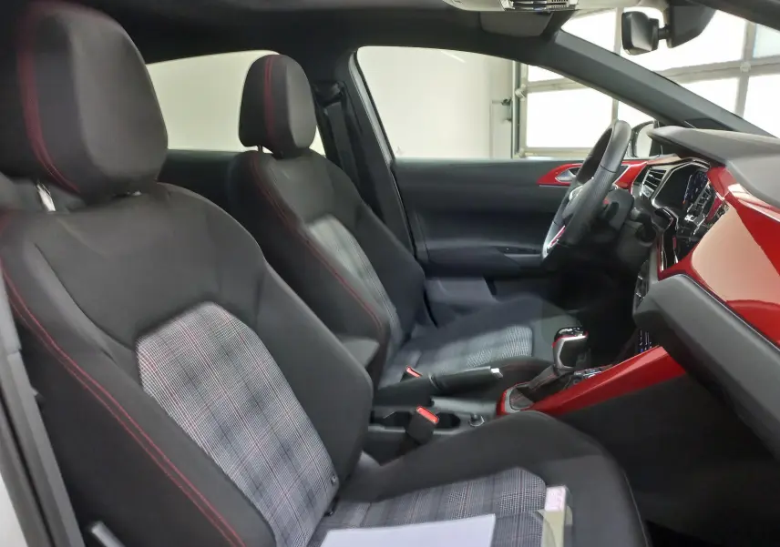 Vue intérieure côté conducteur de la Volkswagen Polo GTI 2024 avec sièges tissu à motif écossais et inserts rouges brillants.