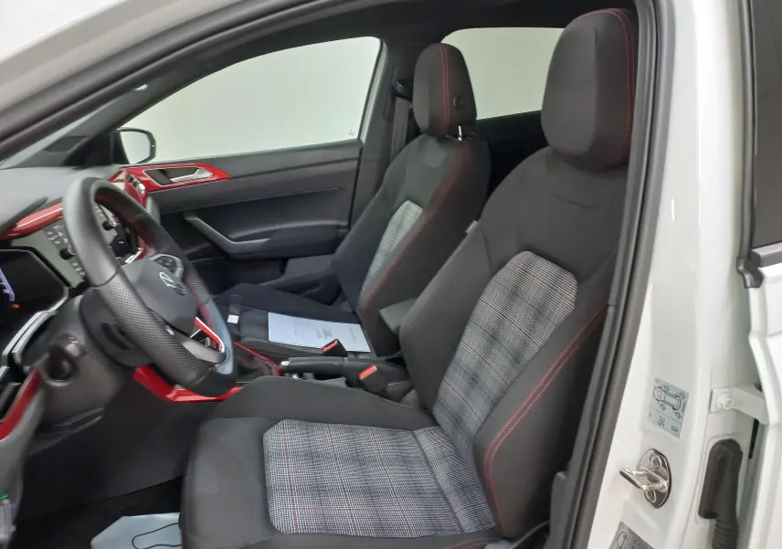 Vue intérieure côté conducteur d'une Volkswagen Polo GTI blanche avec sièges sport à motif écossais et surpiqûres rouges.