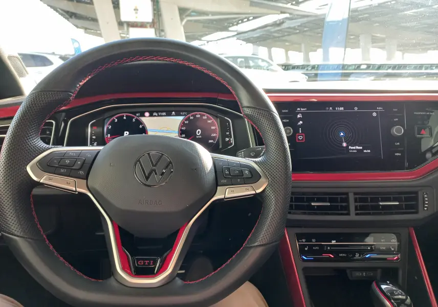 Vue intérieure centrée sur le volant noir avec surpiqûres rouges et tableau de bord numérique de la Volkswagen Polo GTI 2024.