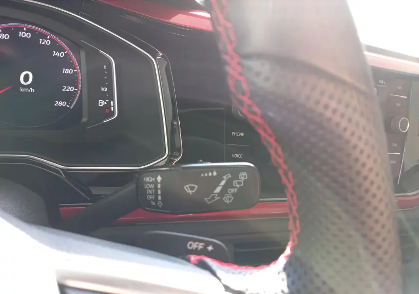 Gros plan intérieur sur le volant perforé avec surpiqûres rouges et le combiné d'instruments numérique de la Volkswagen Polo GTI blanche.