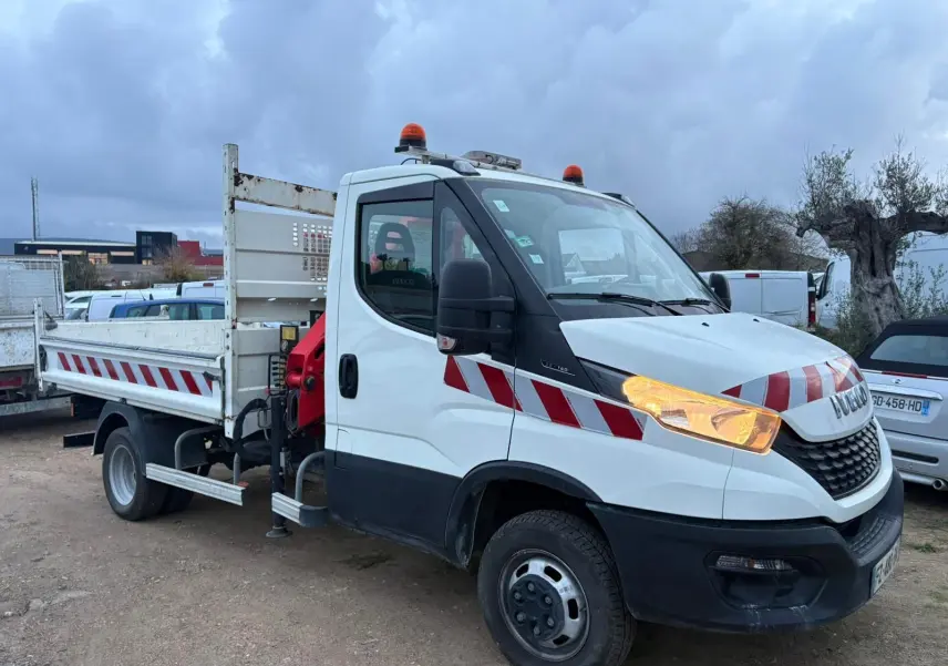 Vue 3/4 avant droite d’un Iveco Daily blanc avec benne, grue rouge Palfinger et bandes rouges réfléchissantes.