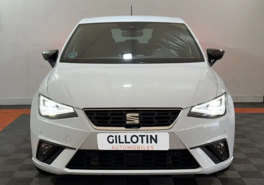 Vue avant d'une SEAT Ibiza 1.0 TSI 110 FR blanche avec phares LED allumés et calandre noire hexagonale.