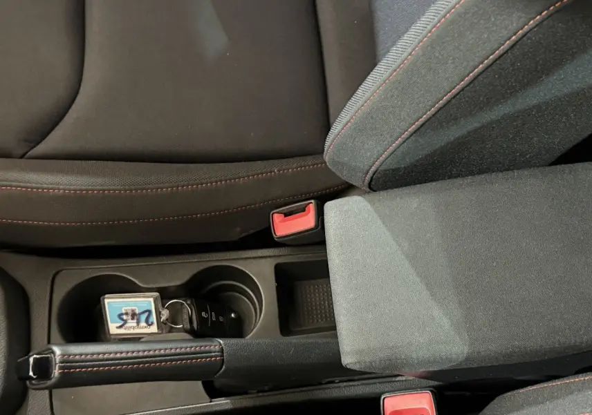Gros plan intérieur sur la console centrale de la SEAT Ibiza blanche, frein à main cuir avec surpiqûres rouges et porte-gobelets.