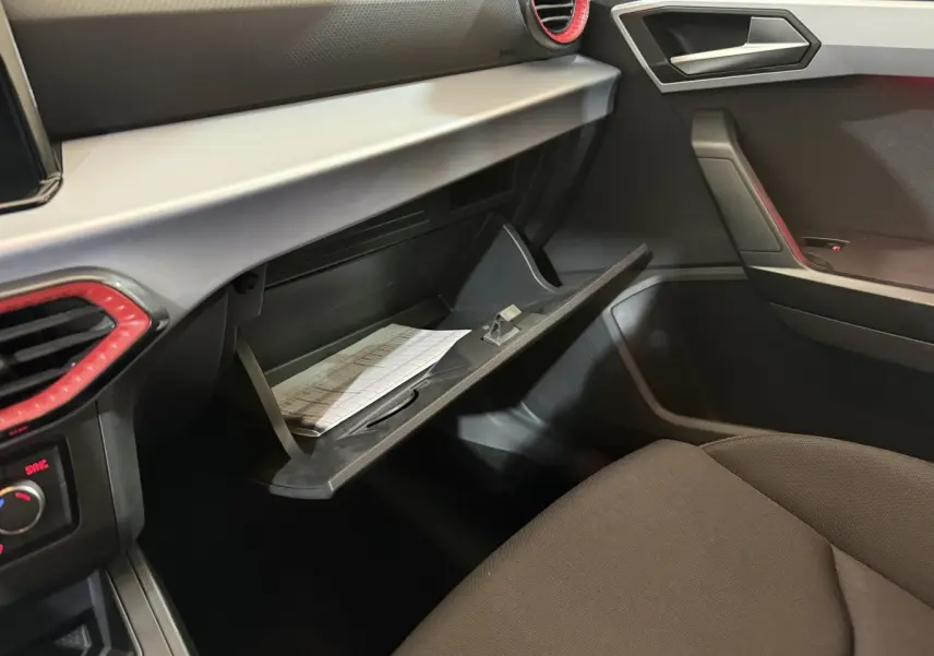 Vue intérieure côté passager de la SEAT Ibiza 2024, boîte à gants ouverte avec documents visibles, ambiance noire et grise.