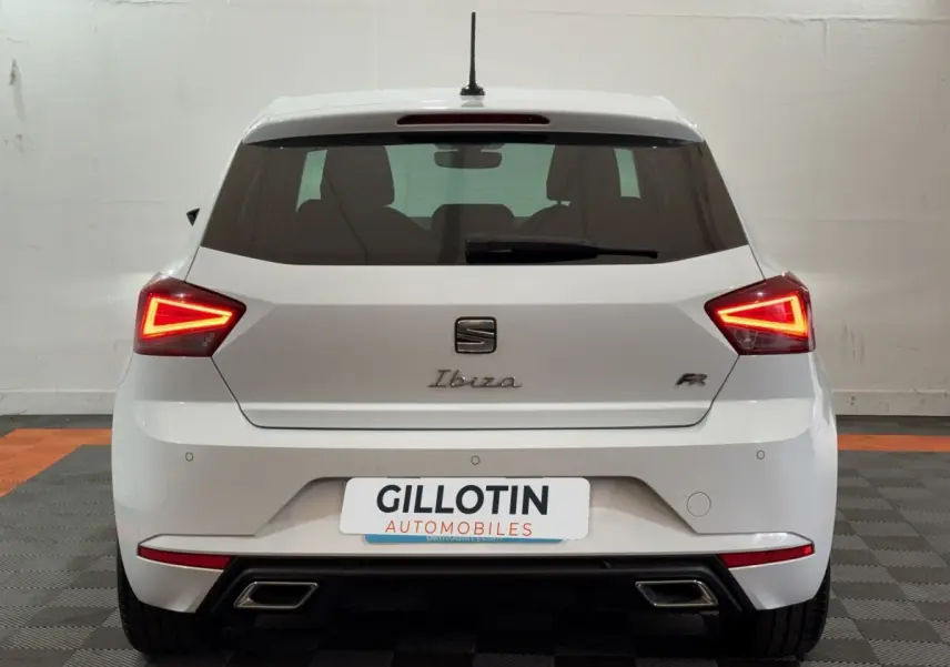 Vue arrière d'une SEAT Ibiza 1.0 TSI 110 FR blanche avec feux LED triangulaires allumés et double sortie d'échappement.
