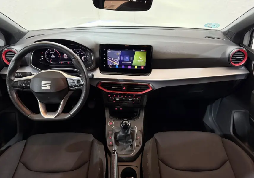 Vue intérieure avant de la SEAT Ibiza 2024, tableau de bord noir avec touches rouges et écran tactile central.