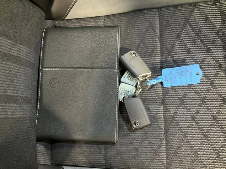 Vue plongeante sur la sellerie noire avec un porte-documents Volkswagen et deux clés du T-ROC 2025 posés dessus.