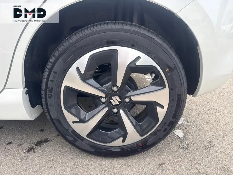 Gros plan sur la jante alu noire et argentée d'une Suzuki Swift blanche, côté roue avant droite.