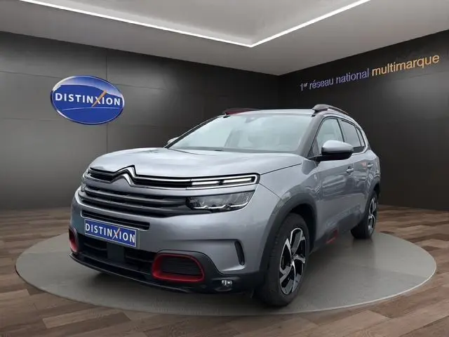 Citroën C5 Aircross gris acier en 3/4 avant droit, avec détails rouges sur le pare-chocs et jantes stylisées.