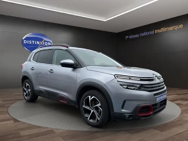 Vue 3/4 avant droite d'un Citroën C5 Aircross gris acier avec détails rouges sur pare-chocs et jantes stylisées.