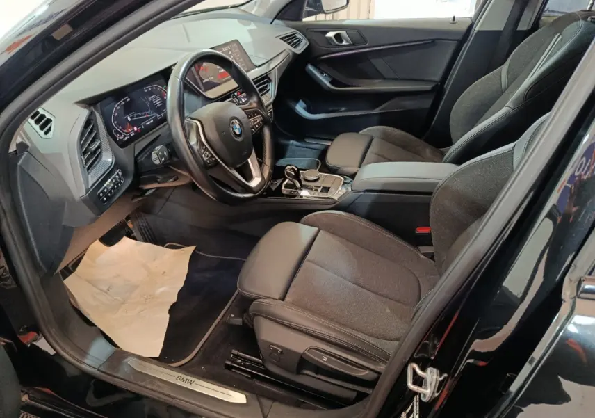 Intérieur noir de la BMW Série 1 118i Edition Sport 2023, vue côté conducteur avec tableau de bord et sièges avant.