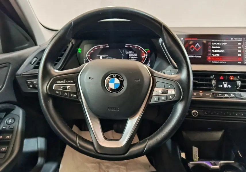 Vue intérieure centrée sur le volant cuir noir et le tableau de bord numérique de la BMW Série 1 118i Edition Sport 2023.