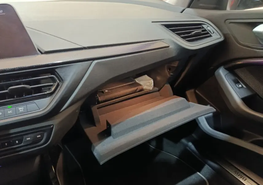 Intérieur BMW Série 1 118i Edition Sport 2023, vue côté passager sur boîte à gants ouverte et tableau de bord noir.