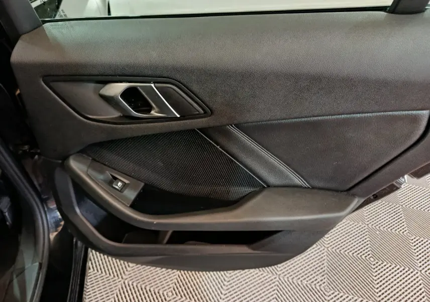 Gros plan sur la porte intérieure côté gauche noire de la BMW Série 1 118i Edition Sport avec poignée argentée et commande de vitre.