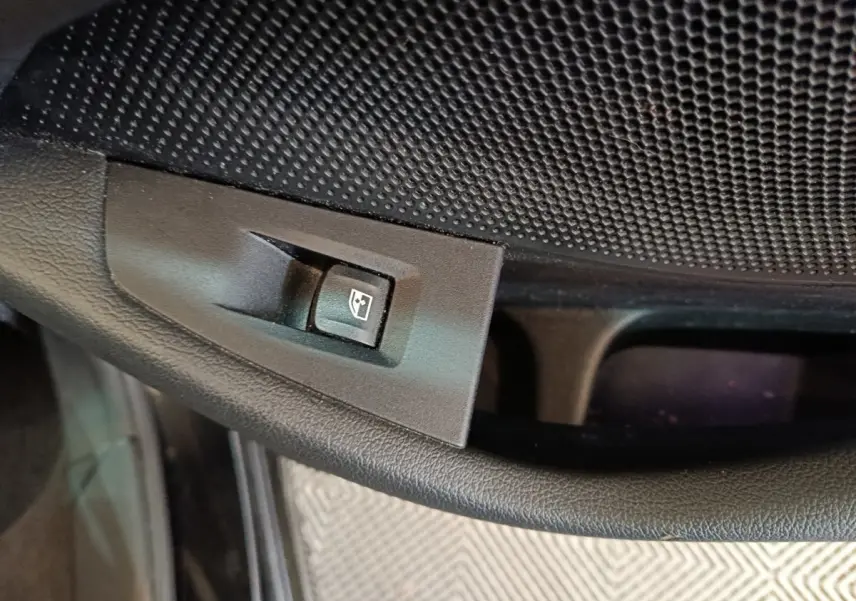 Gros plan sur le bouton de commande de lève-vitre côté conducteur dans l'habitacle noir de la BMW Série 1.