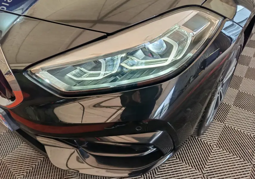 Gros plan sur le phare avant droit noir brillant d'une BMW Série 1 118i Edition Sport 2023.