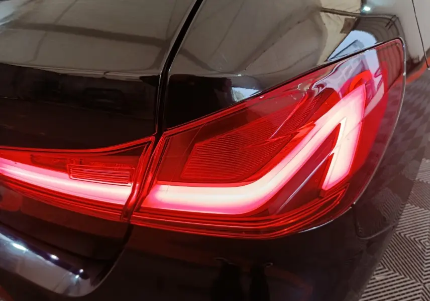 Gros plan sur le feu arrière droit allumé d’une BMW Série 1 118i Edition Sport noire, finition brillante.