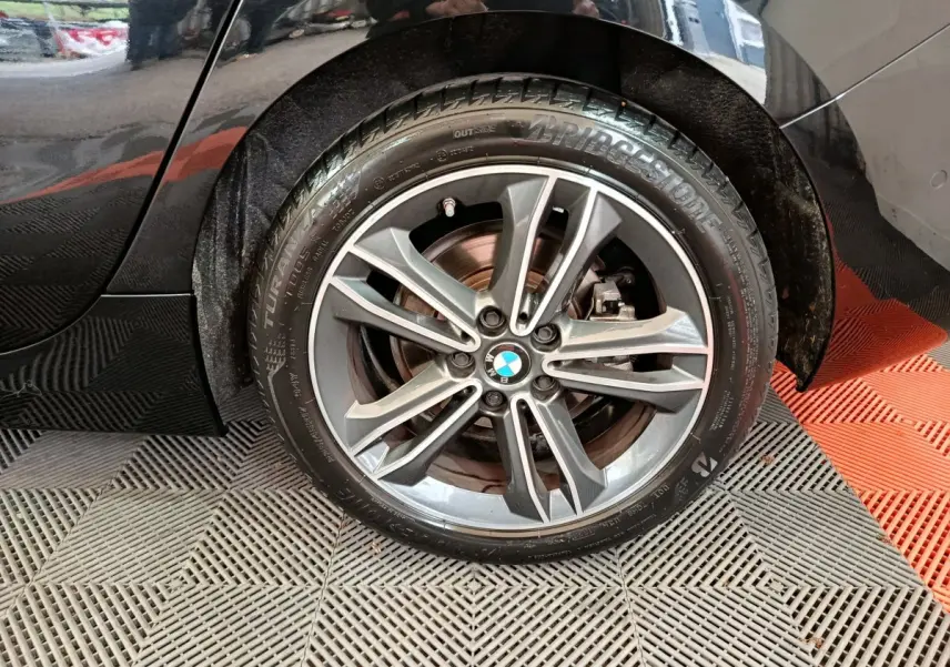 Gros plan sur la roue arrière droite noire d'une BMW Série 1 118i Edition Sport avec jante alliage et logo BMW visible.