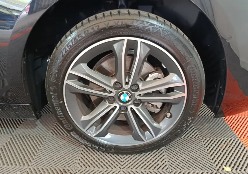Gros plan sur la roue avant gauche noire d’une BMW Série 1 118i Edition Sport avec jante alliage grise.