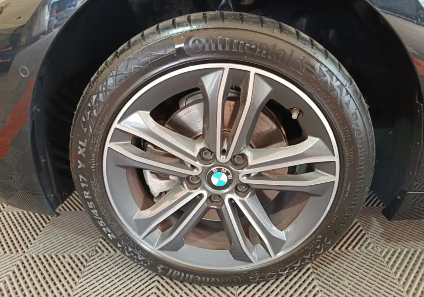 Gros plan sur la roue avant droite noire d'une BMW Série 1 118i Edition Sport avec jante alliage gris foncé.