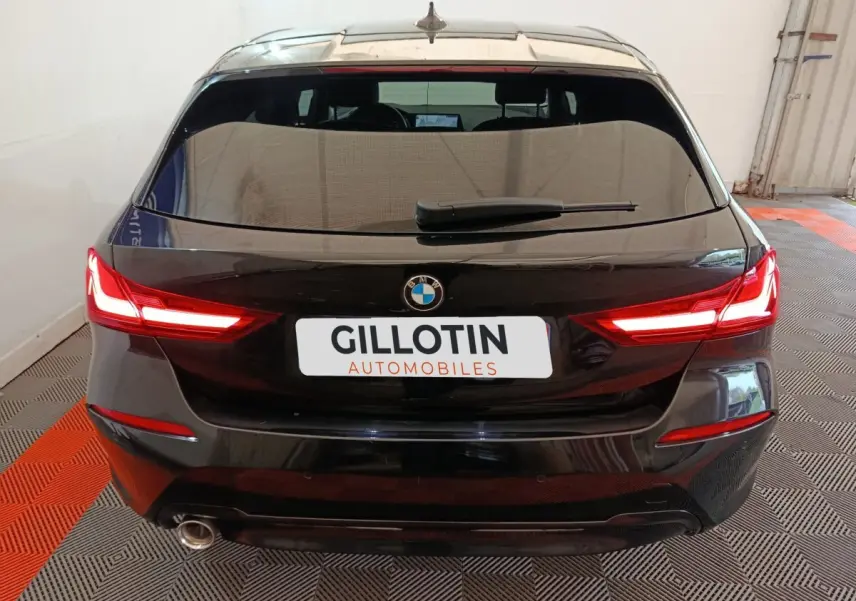 Vue arrière d’une BMW Série 1 118i Edition Sport noire avec feux LED allumés dans un garage.