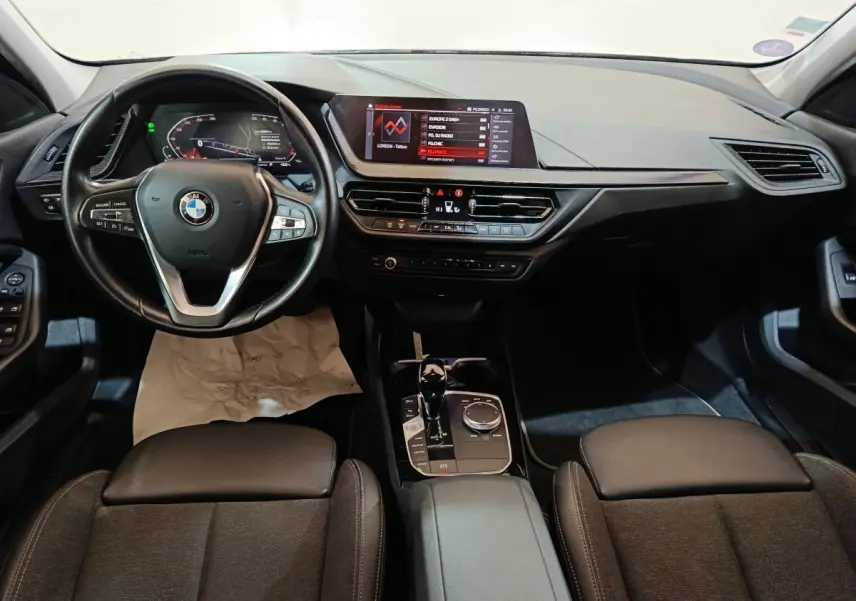 Vue intérieure avant de la BMW Série 1 118i Edition Sport 2023, tableau de bord noir avec écran tactile et volant cuir multifonctions.