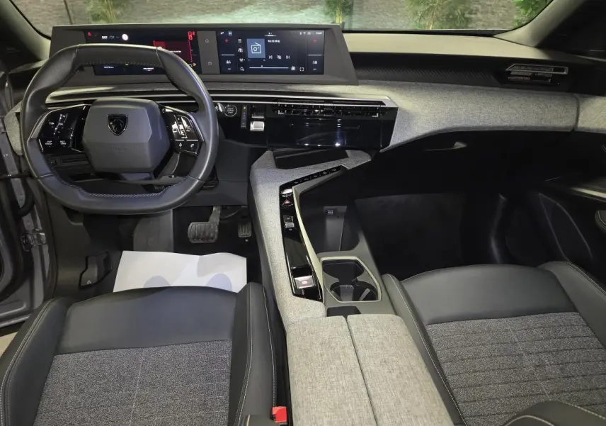 Intérieur avant du Peugeot 3008 gris 2025, tableau de bord avec double écran HD et sellerie tissu gris et cuir noir.