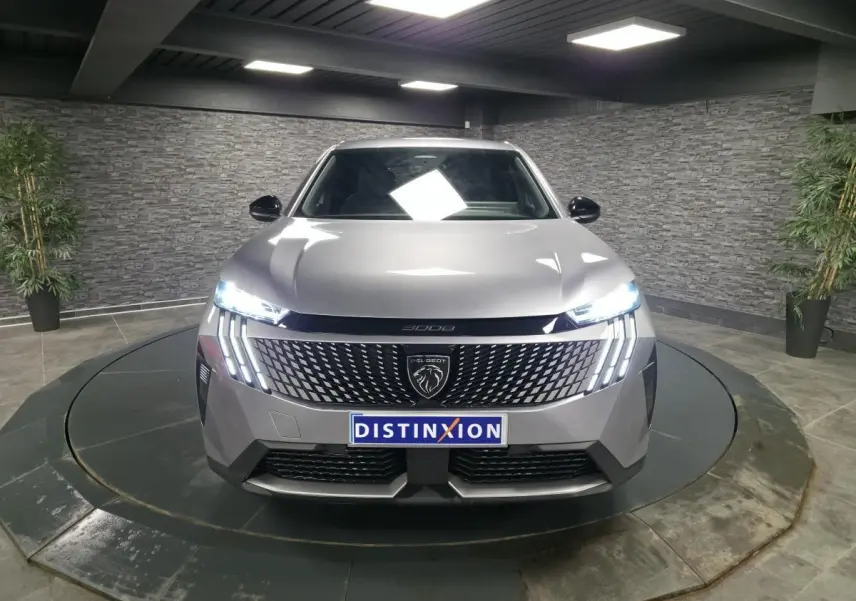 Peugeot 3008 gris vue de face, avec calandre noire laquée et feux LED allumés en intérieur showroom.