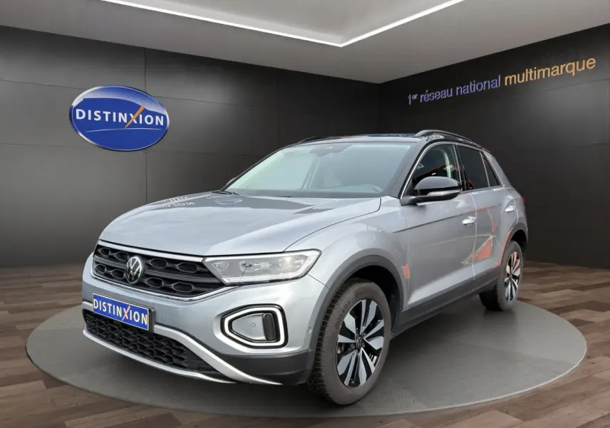 Volkswagen T-Roc gris clair en 3/4 avant droit, avec jantes alliage et calandre noire distinctive.