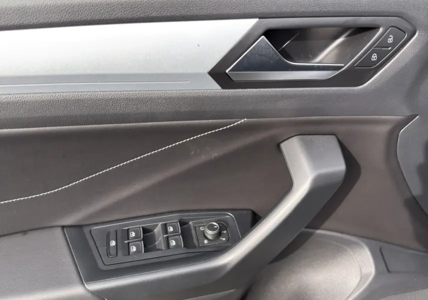 Gros plan sur la porte côté conducteur du Volkswagen T-Roc gris clair, montrant les commandes des vitres et la poignée intérieure.