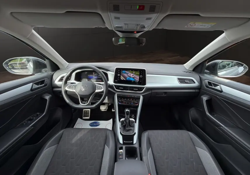 Vue intérieure avant du Volkswagen T-Roc gris clair 2025, avec tableau de bord numérique et écran tactile central.