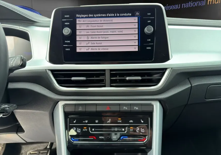 Vue intérieure du tableau de bord du Volkswagen T-Roc 2025, écran tactile central affichant les réglages d'aide à la conduite.