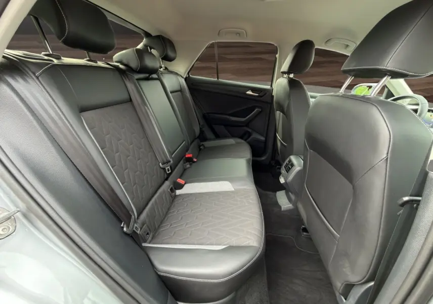Vue intérieure arrière du Volkswagen T-Roc 2025 gris clair, montrant la banquette 3 places en tissu et cuir avec ceintures de sécurité.