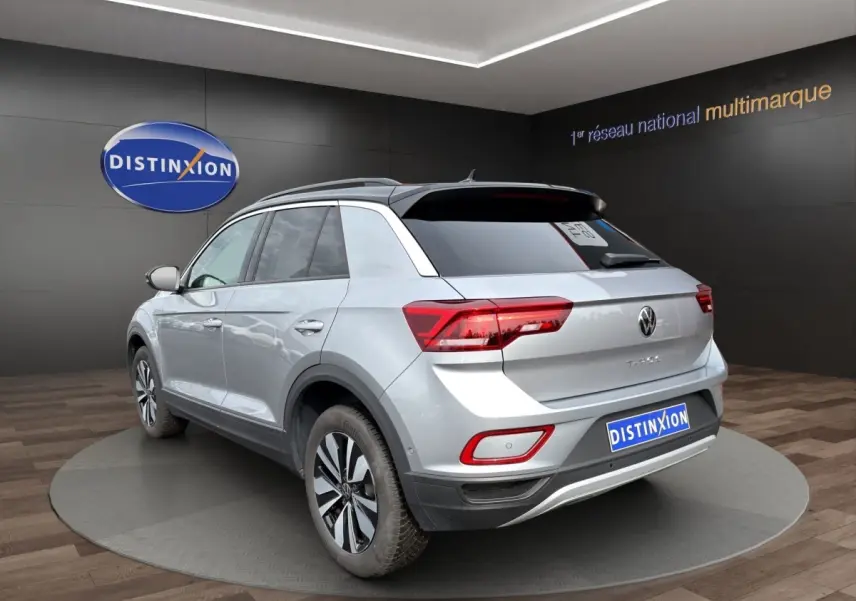 Vue 3/4 arrière d'un Volkswagen T-Roc gris clair avec attelage amovible dans un showroom.