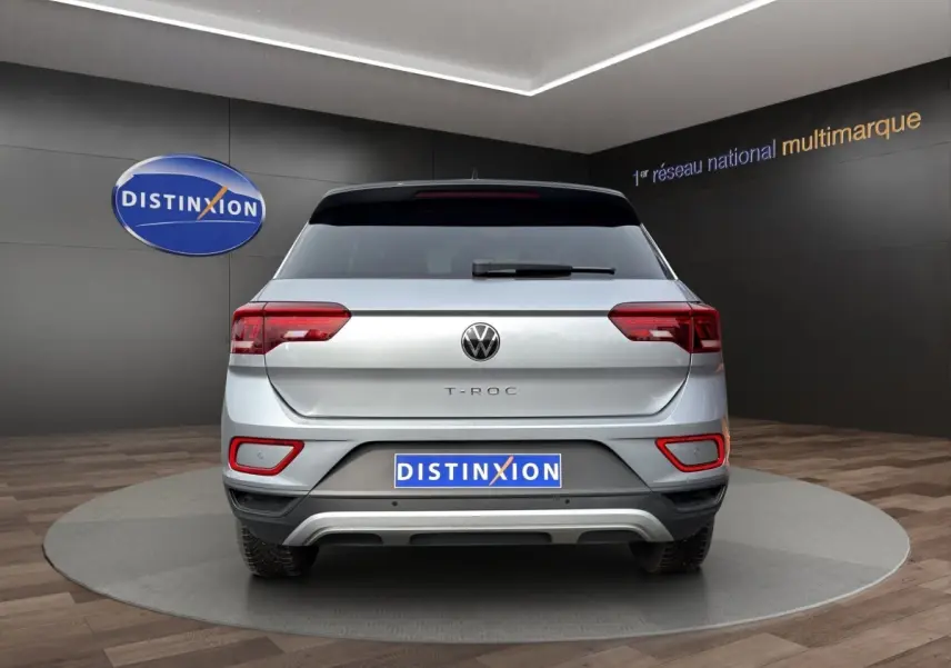 Vue arrière d'un Volkswagen T-Roc gris clair 2025 avec feux LED et attelage amovible visible en showroom.