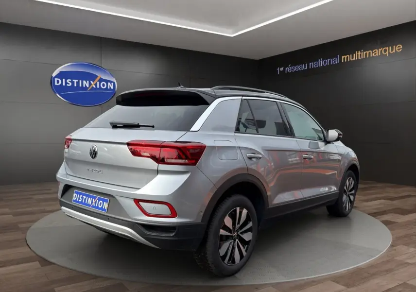 Vue 3/4 arrière droite d'un Volkswagen T-Roc gris clair avec jantes noires et grises, dans un showroom.